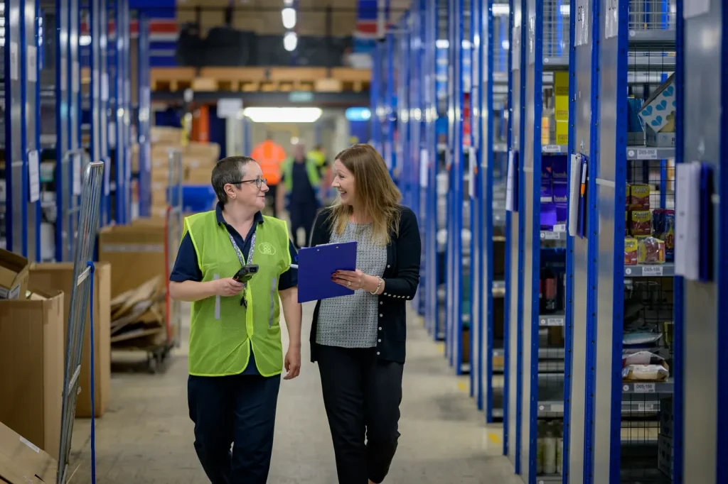 Two warehouse staff walking down an aisle with a scanner and a clipboard